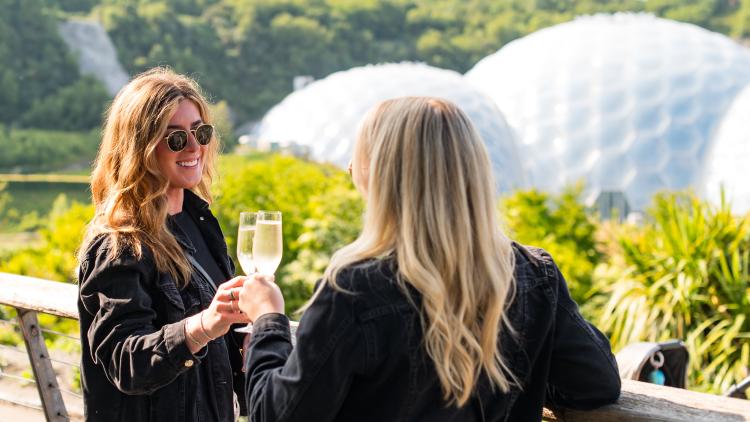 Two women chinking glasses with the Eden Project Biomes in the background