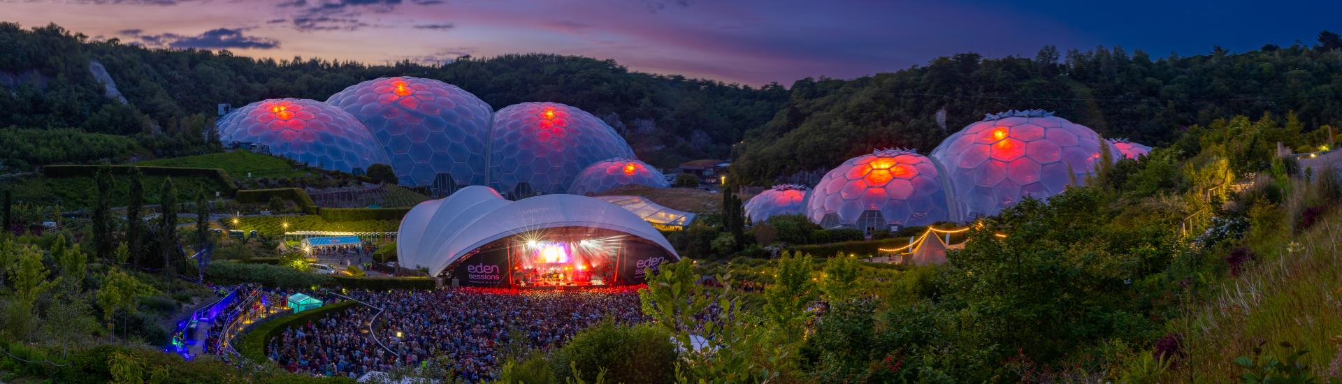 Wide view of Eden Sessions with blue and purple evening sky and the Biomes lit up red